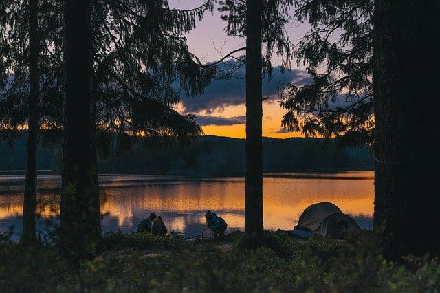 Camping sunset gathering of friends by lake with trees